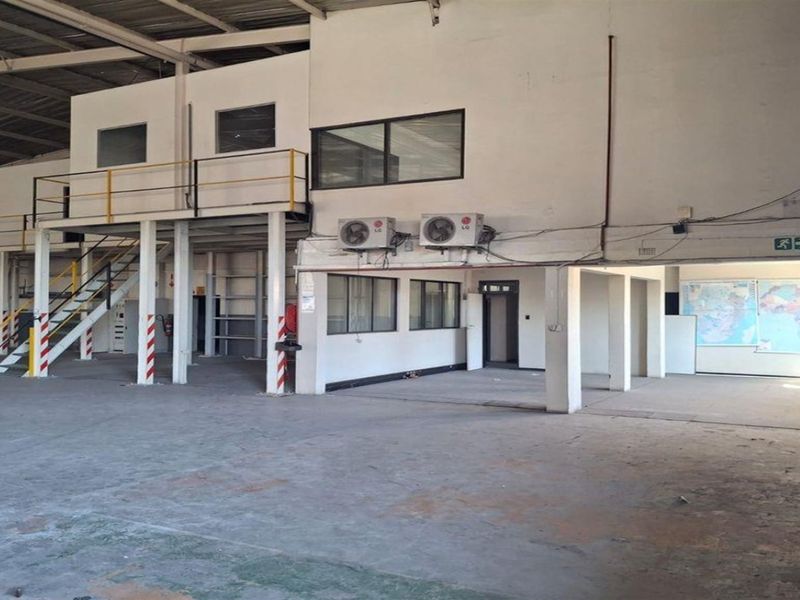 Spacious industrial warehouse interior featuring a mezzanine level, steel staircase, exposed roof trusses, and wall-mounted air conditioning units.