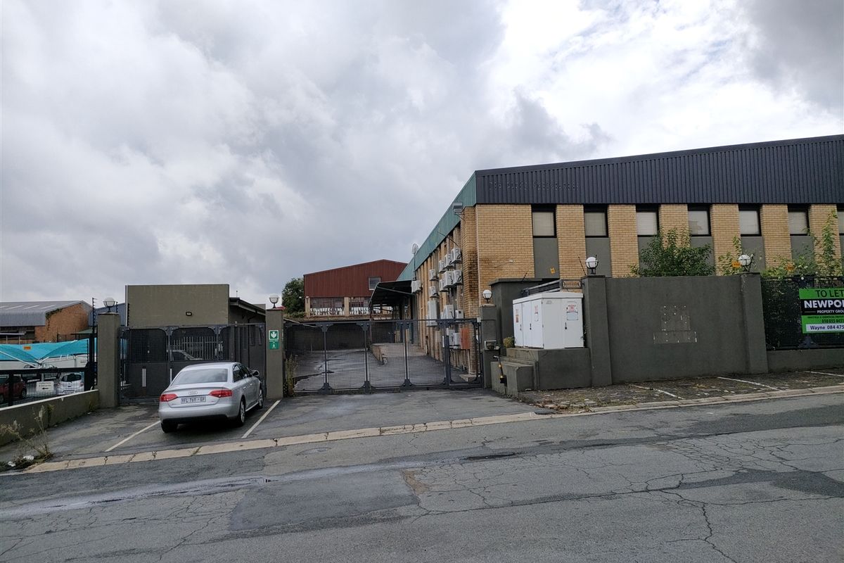 Front exterior view of an industrial property featuring a gated entrance, asphalt driveway, and brick facade with multiple external air conditioning units.