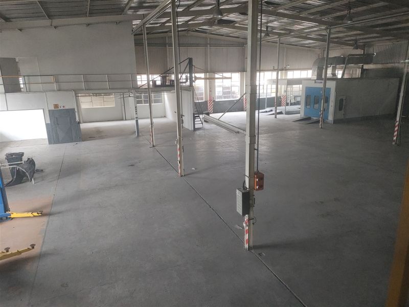 Spacious industrial warehouse featuring concrete flooring, exposed steel roof structure, mezzanine level, and a dedicated spray booth area.