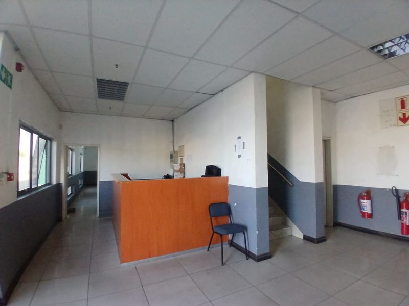 Industrial reception area featuring a built-in service counter, tiled flooring, suspended ceiling, and direct access to a staircase and adjacent hallway.