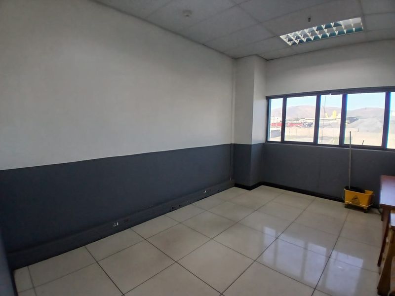 A functional office space featuring tiled flooring, a suspended ceiling with recessed lighting, and large windows providing natural light and exterior views.