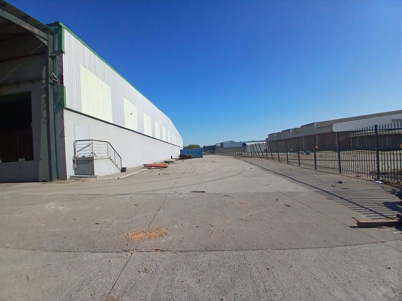 Spacious industrial yard area featuring concrete paving, perimeter steel fencing, and access to a large warehouse structure.