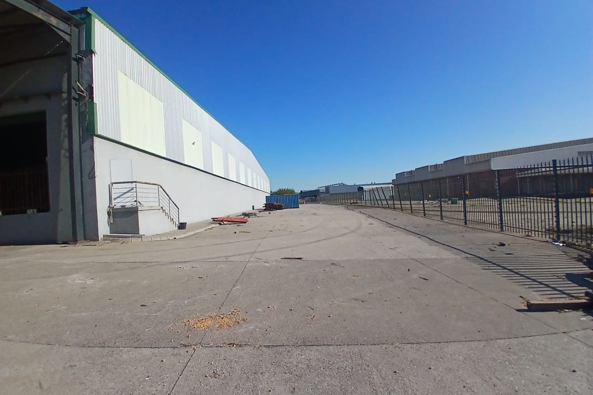 Spacious industrial yard area featuring concrete paving, perimeter steel fencing, and access to a large warehouse structure.