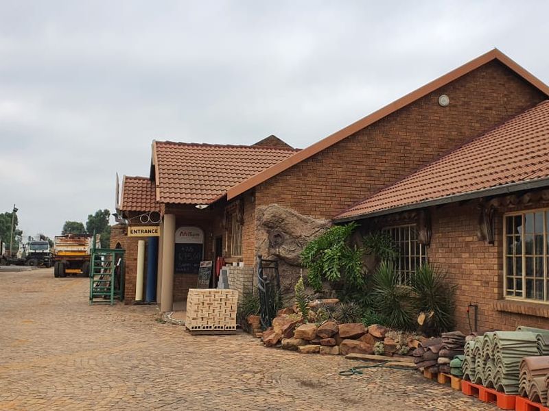 Exterior view of a commercial brick building featuring a tiled roof, paved yard area, and designated entrance.