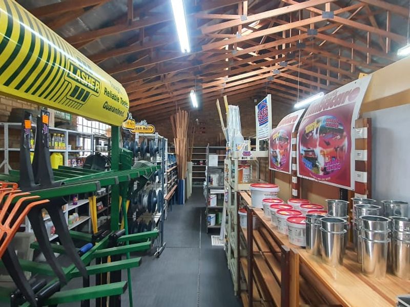Interior view of a retail hardware store featuring exposed timber roof trusses, fluorescent lighting, and extensive built-in shelving units for product display.