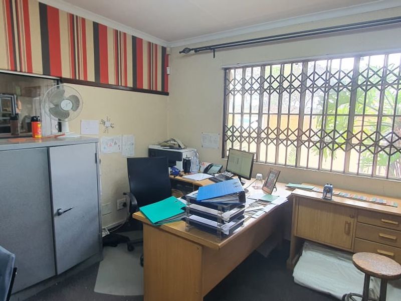 Functional office space featuring built-in cabinetry, large window with security gate, and neutral wall finishes suitable for a professional business environment.