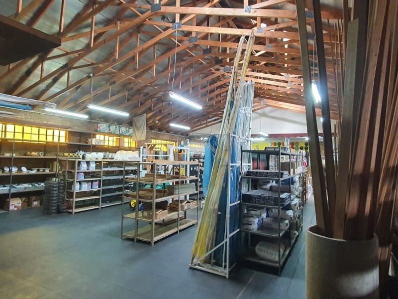Spacious commercial warehouse or retail area featuring high exposed timber roof trusses, industrial lighting, and extensive built-in shelving units for storage or display.