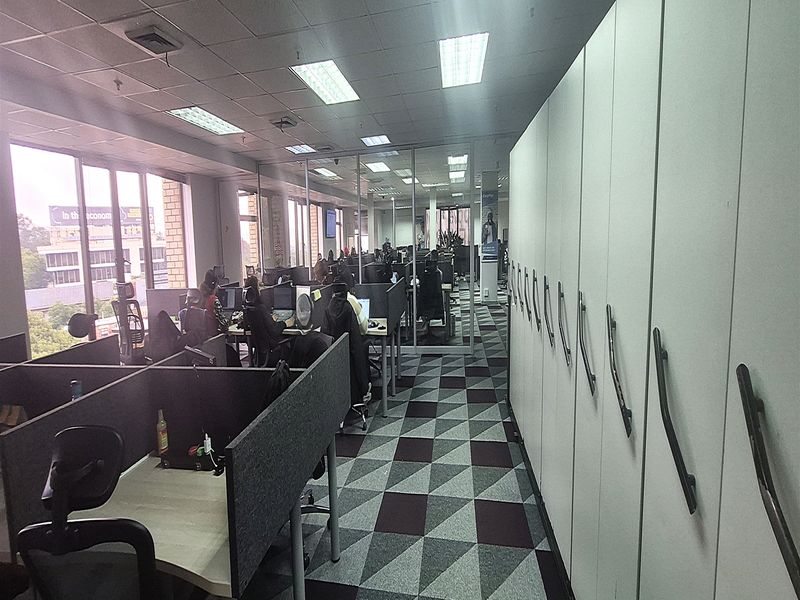 Open-plan office space featuring modular workstations, built-in storage cabinetry, carpeted flooring, and large windows providing natural light.