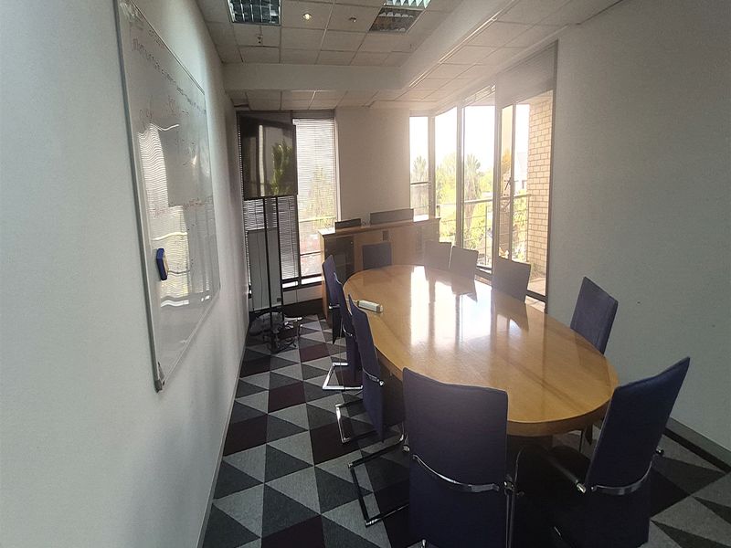 A functional office meeting room featuring a large conference table, patterned carpet tiles, suspended ceiling with recessed lighting, and access to a balcony.