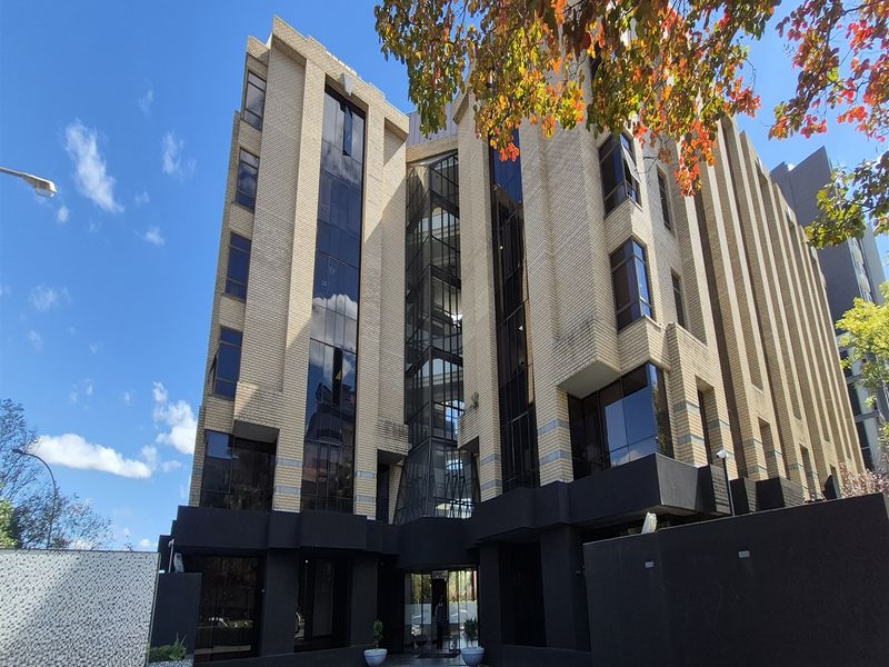 Modern multi-story office building featuring a distinctive brick and glass facade with a paved entrance area.