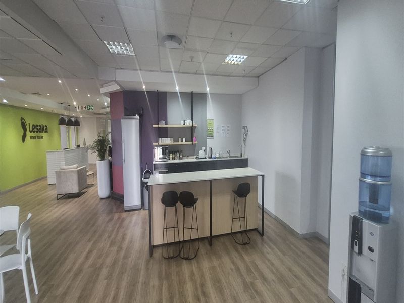 Modern office space featuring a functional kitchenette area with built-in shelving, laminate flooring, and a suspended ceiling with recessed lighting.