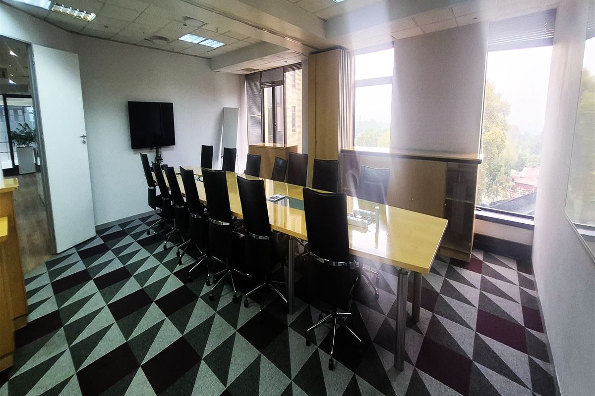A professional office boardroom featuring a large central table, built-in storage cabinetry, patterned carpet flooring, and ample natural light from large windows.