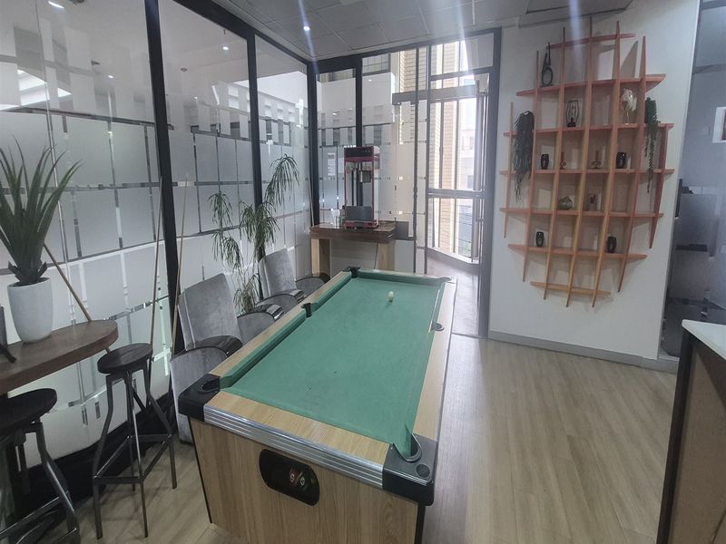 A modern office breakout area featuring glass partition walls, laminate flooring, and built-in decorative wall shelving.