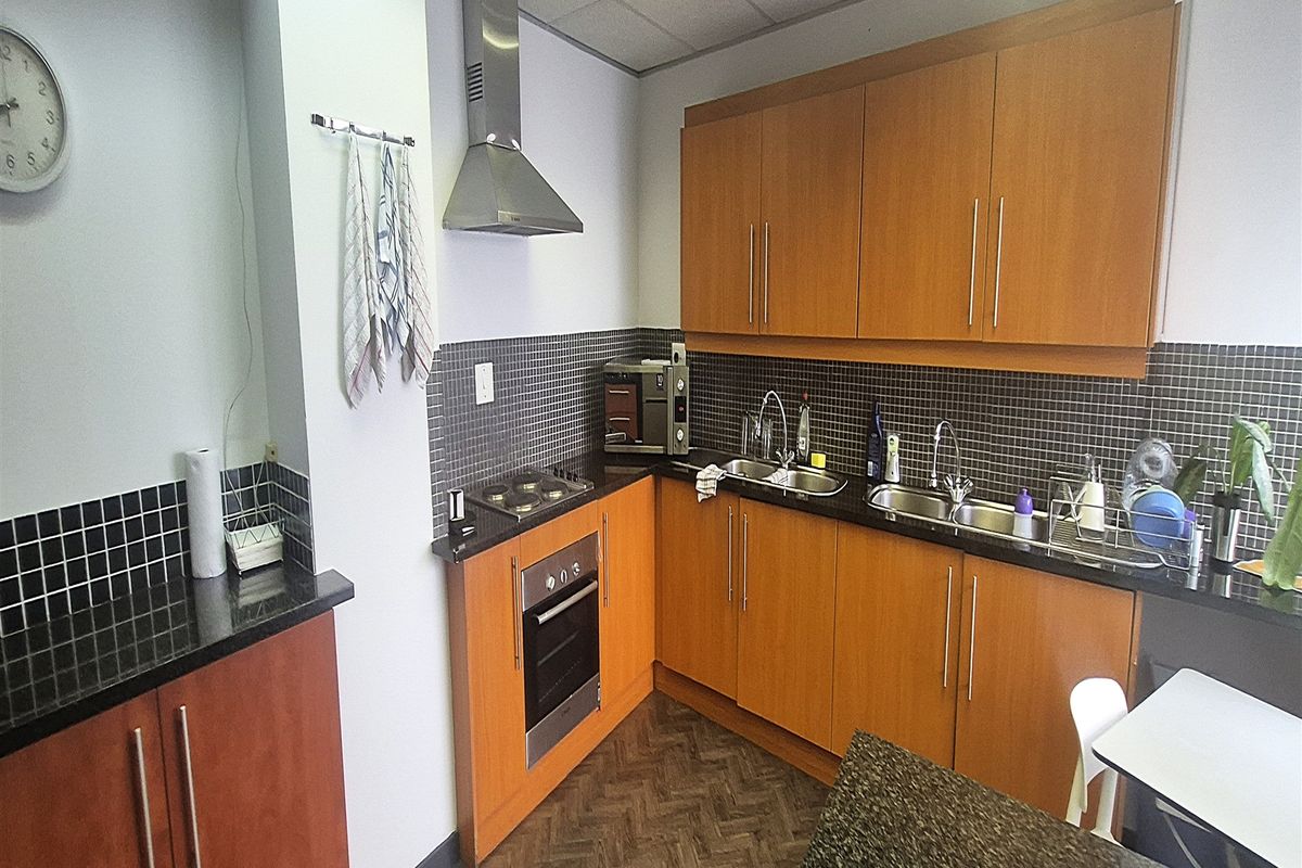 A functional office kitchenette featuring wood-finish cabinetry, granite countertops, a built-in oven, gas hob, and a tiled backsplash.