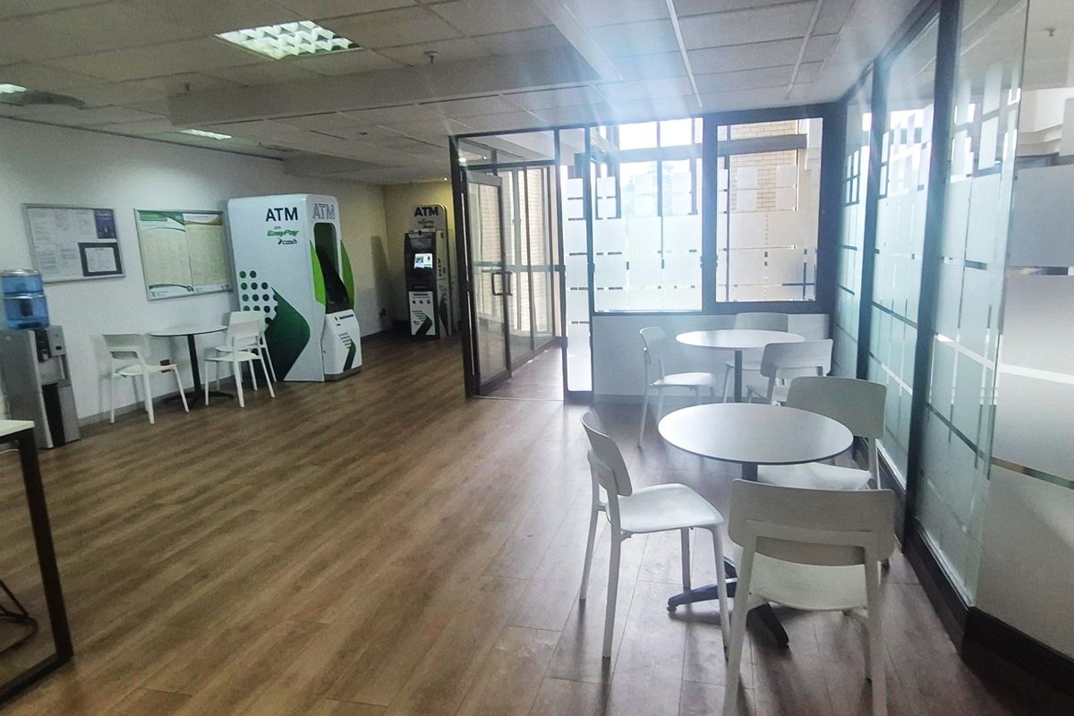 Modern office lobby or waiting area featuring glass partitions, suspended ceilings, and wood-look laminate flooring with integrated ATM facilities.