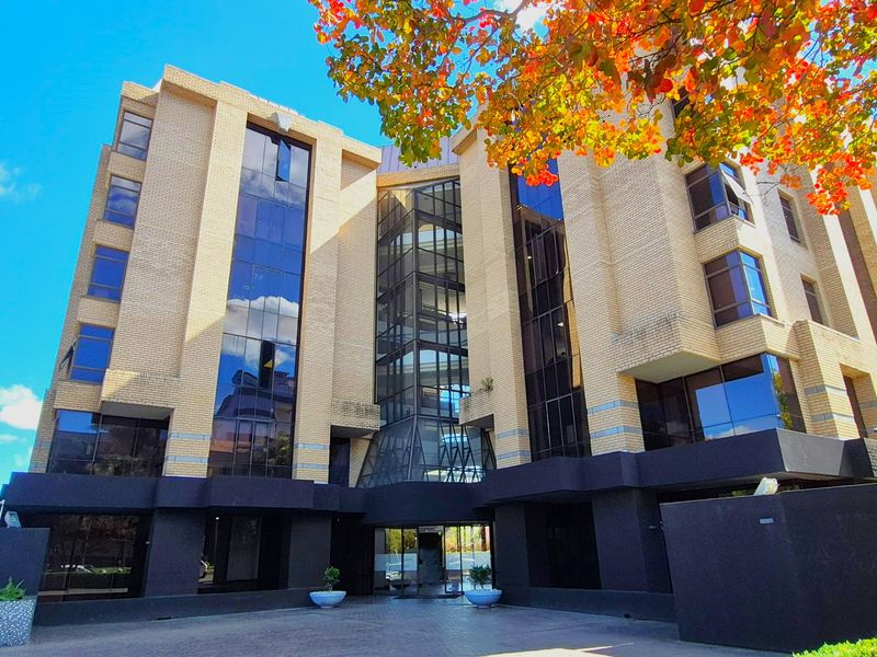 A modern multi-story office building featuring a prominent brick facade, extensive glass curtain walling, and a paved ground-level entrance area.