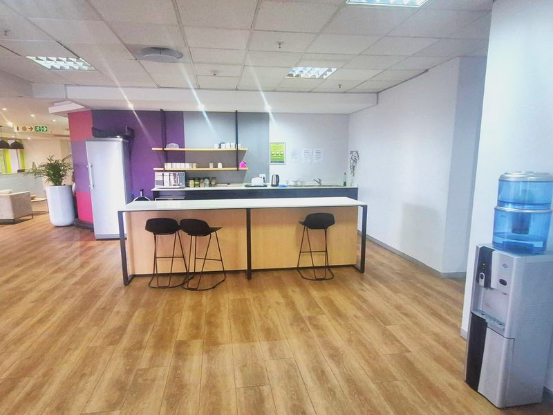Office kitchenette area featuring a breakfast counter, laminate flooring, and a suspended ceiling with integrated lighting.