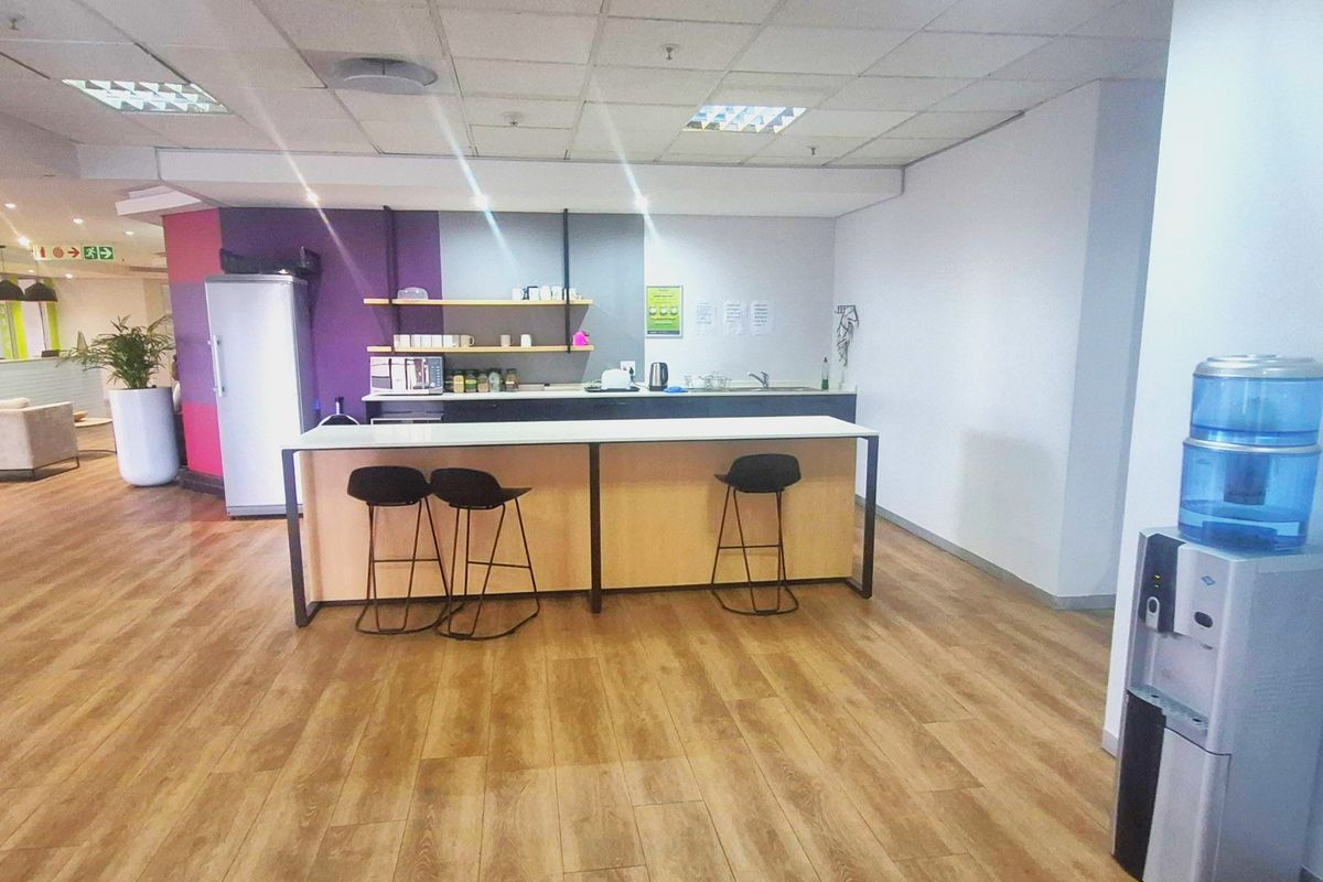 Office kitchenette area featuring a breakfast counter, laminate flooring, and a suspended ceiling with integrated lighting.