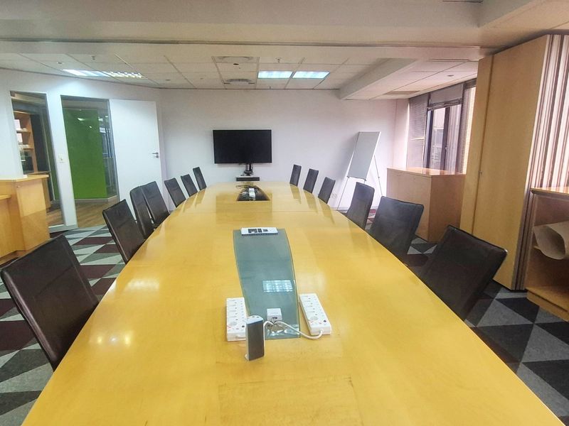 A professional boardroom featuring a large central conference table, suspended ceiling with recessed lighting, and built-in storage cabinetry.