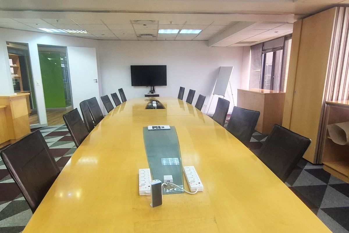 A professional boardroom featuring a large central conference table, suspended ceiling with recessed lighting, and built-in storage cabinetry.