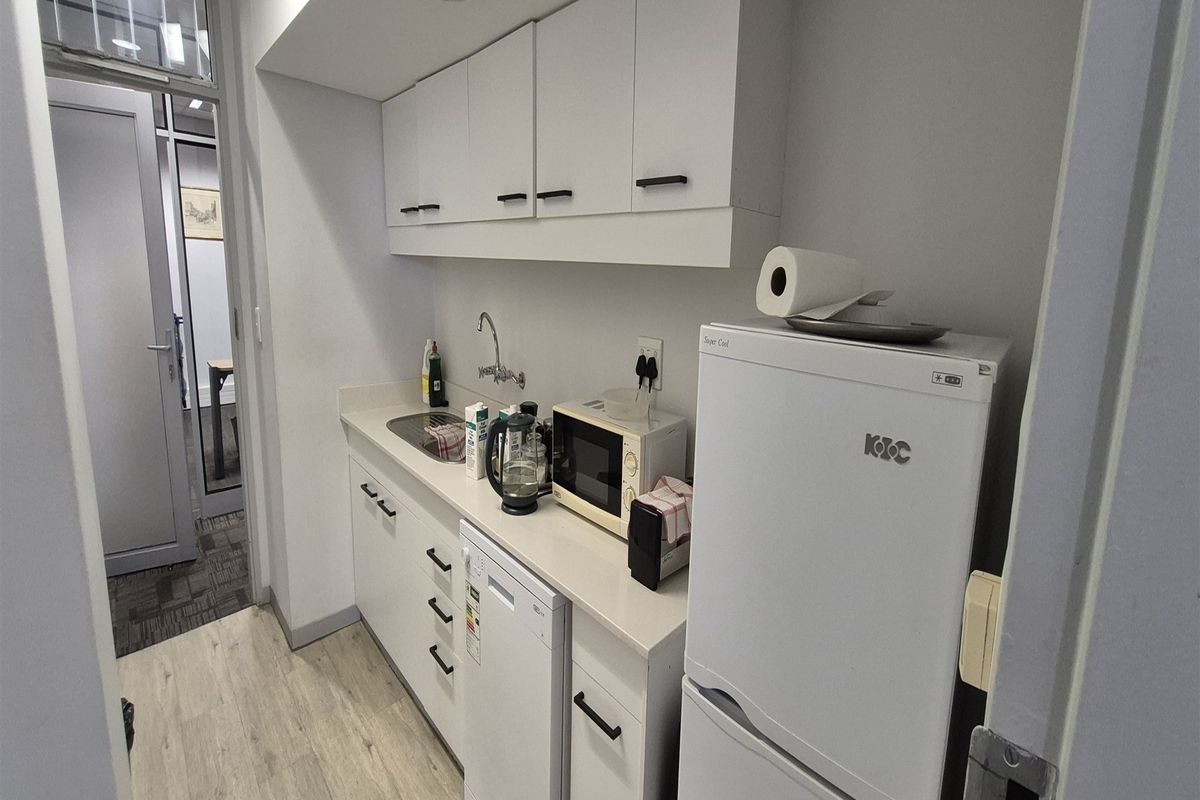 A compact office kitchenette featuring white built-in cabinetry, a laminate countertop, and a stainless steel sink, providing essential utility for a workspace.