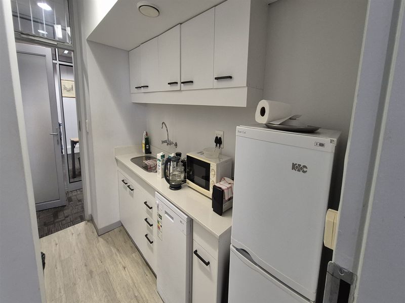 A compact office kitchenette featuring white built-in cabinetry, a laminate countertop, and a stainless steel sink, providing essential utility for a workspace.