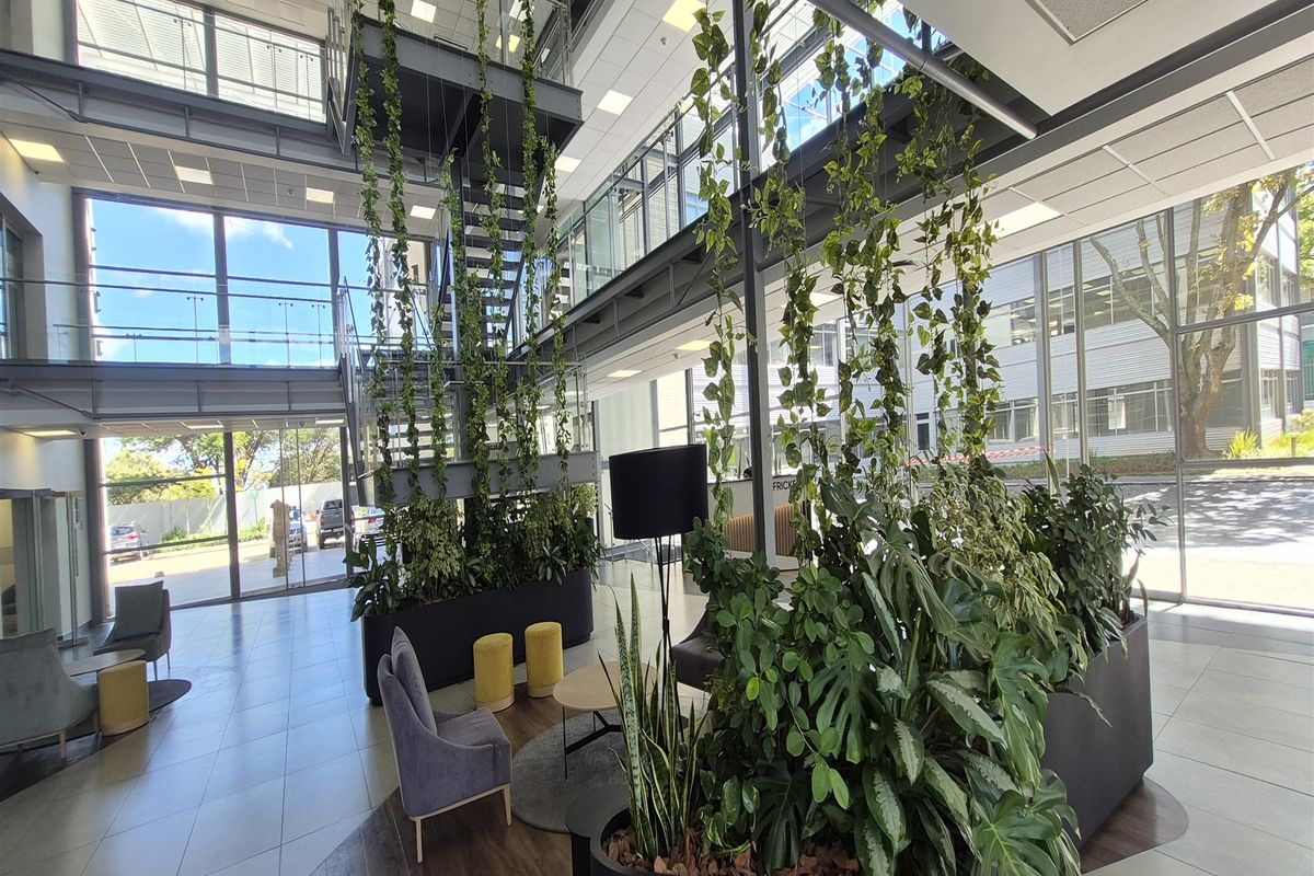 Modern office building entrance lobby featuring a double-volume atrium, steel staircase, extensive glass facade, and contemporary tiled flooring.