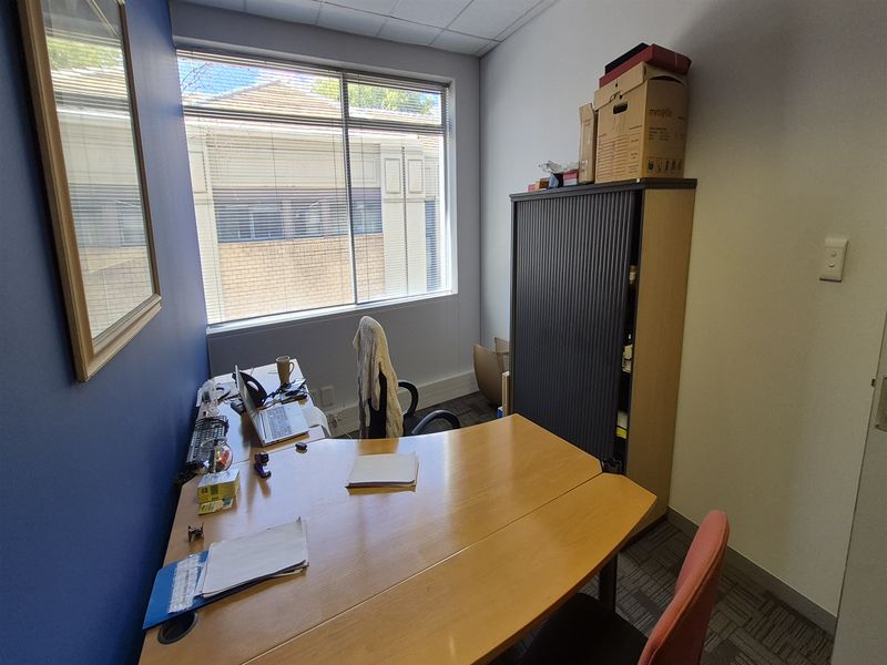 A functional office space featuring carpet tiles, a suspended ceiling, and a large window with venetian blinds providing natural light.