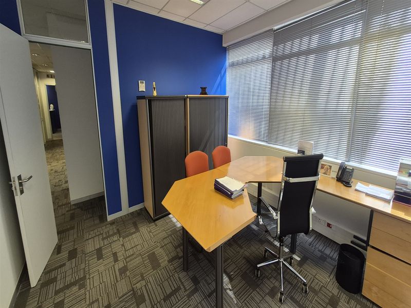 A functional office space featuring carpet tiles, a suspended ceiling, venetian blinds, and built-in storage cabinetry.