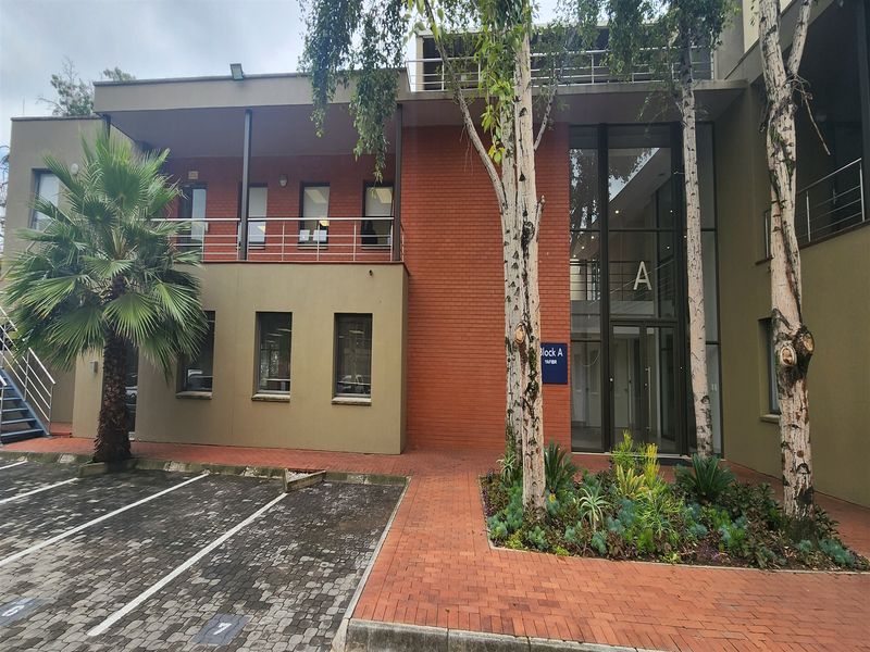 Front elevation of a modern office building featuring a brick facade, glass entrance, and paved parking area.