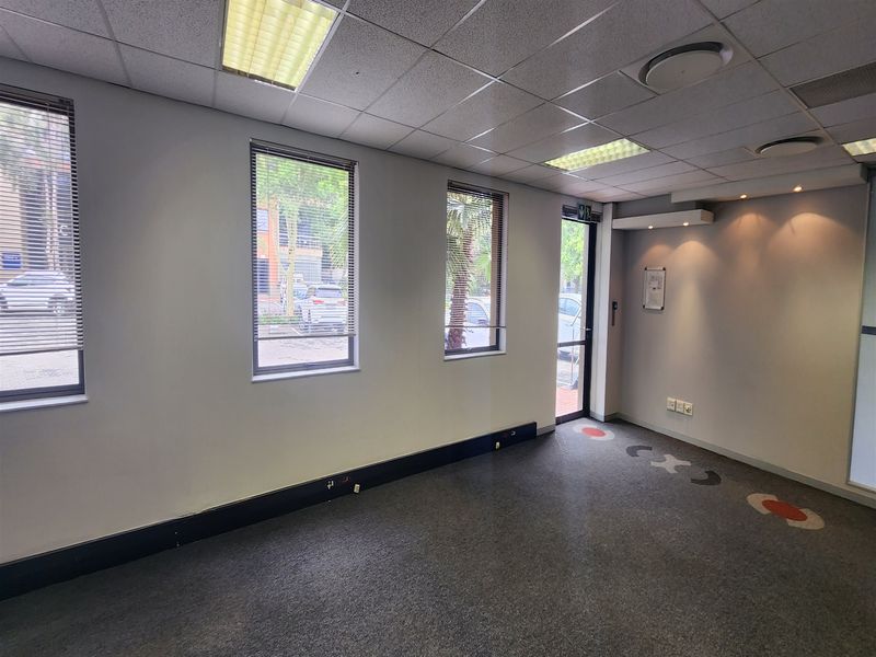 A vacant office space featuring a suspended ceiling with recessed lighting, carpeted flooring, and large windows with venetian blinds.