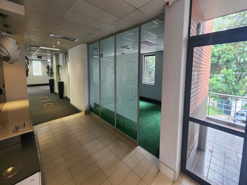 Modern office interior featuring a glass partition wall, suspended ceiling, and a mix of tiled and carpeted flooring with access to an outdoor balcony.