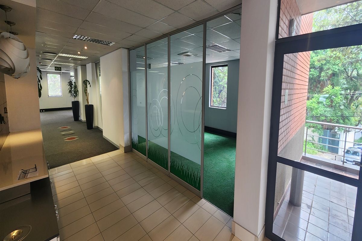 Modern office interior featuring a glass partition wall, suspended ceiling, and a mix of tiled and carpeted flooring with access to an outdoor balcony.