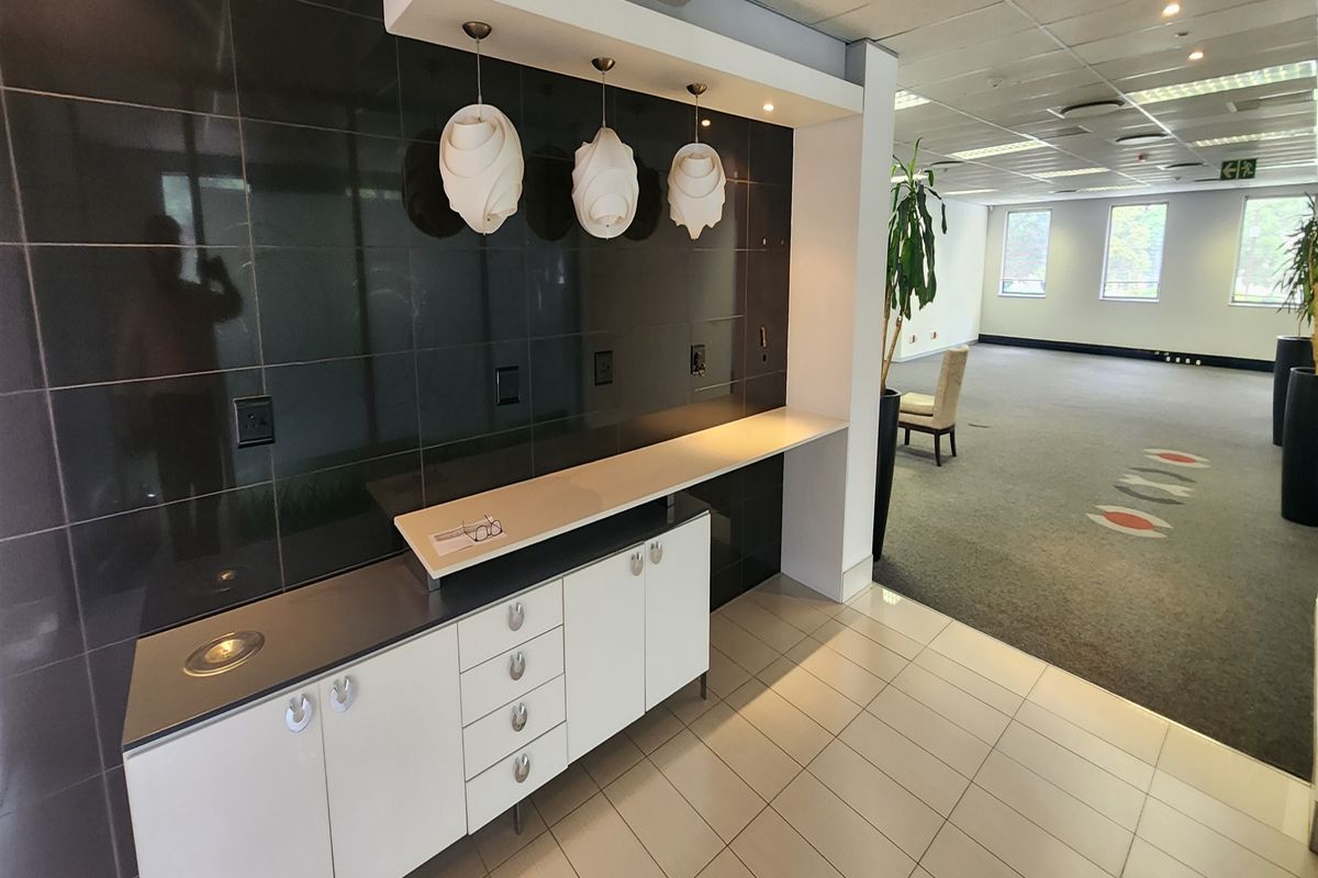 A professional office space featuring a built-in kitchenette or refreshment station with modern cabinetry, tiled flooring, and a suspended ceiling with recessed lighting.