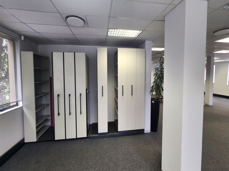 An office space featuring a suspended ceiling, recessed lighting, carpeted flooring, and built-in storage shelving units.