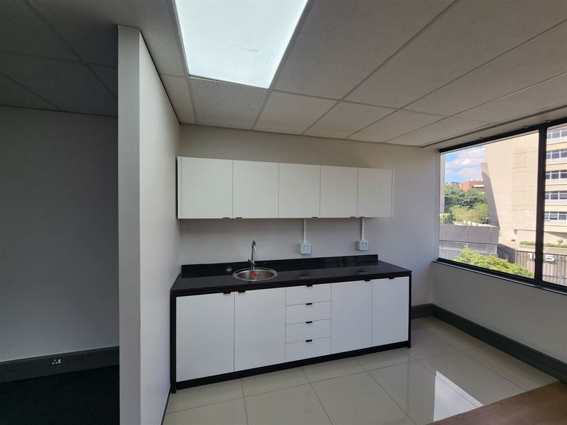 A clean, modern office kitchenette featuring white cabinetry, black granite countertops, a stainless steel sink, and large windows providing natural light.