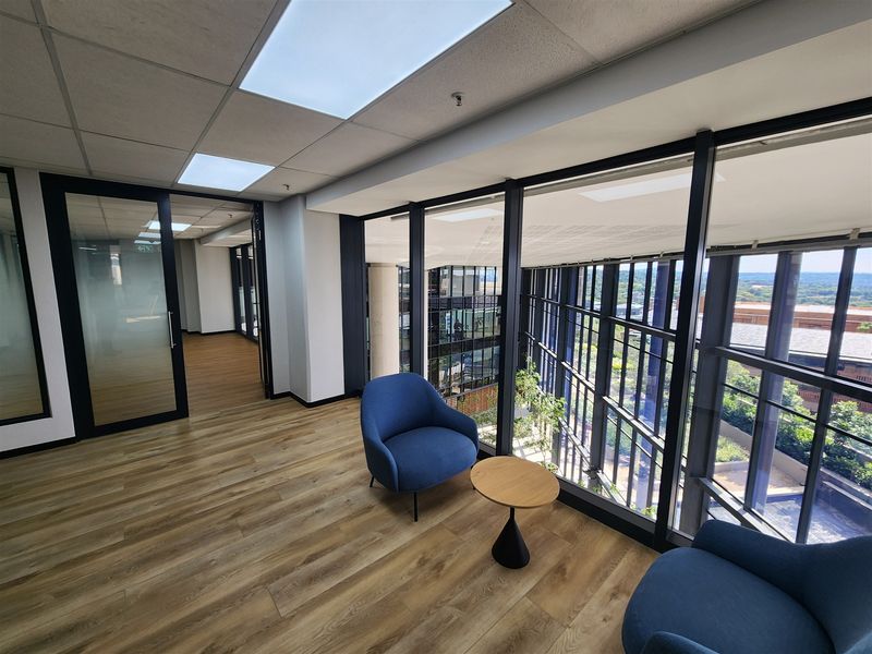 Modern office space featuring floor-to-ceiling windows, suspended ceilings with recessed lighting, and high-quality laminate flooring with a view of the building atrium.