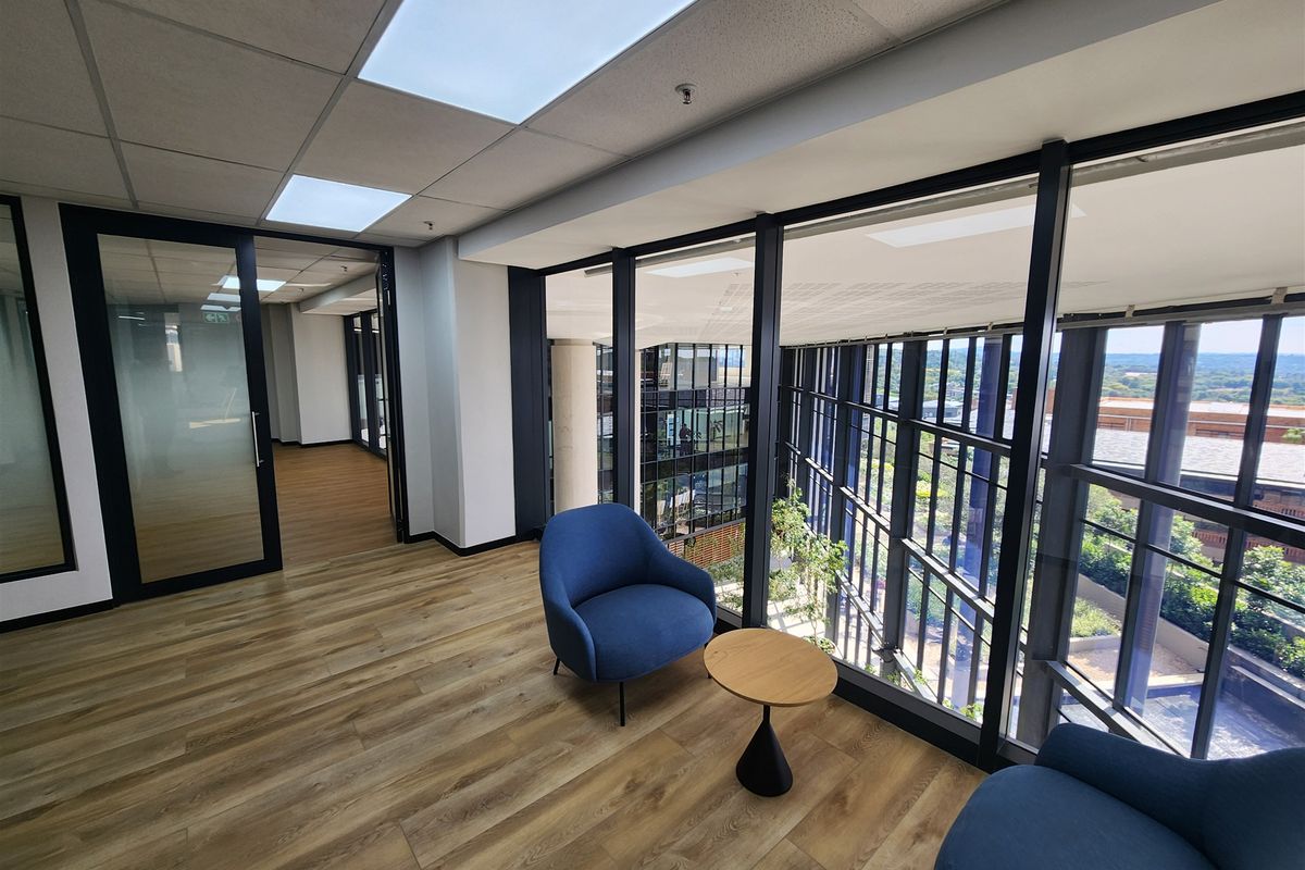 Modern office space featuring floor-to-ceiling windows, suspended ceilings with recessed lighting, and high-quality laminate flooring with a view of the building atrium.