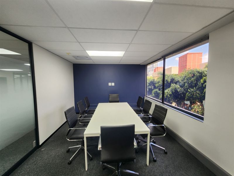 A professional office meeting room featuring a large window with natural light, a glass partition wall, and a modern suspended ceiling.