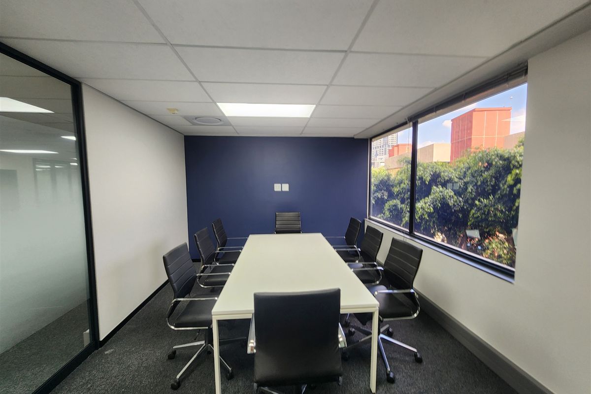 A professional office meeting room featuring a large window with natural light, a glass partition wall, and a modern suspended ceiling.