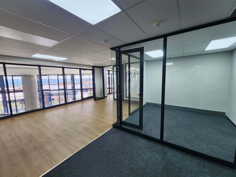Modern open-plan office space featuring glass partitions, suspended ceilings with recessed lighting, and a combination of laminate and carpet flooring.