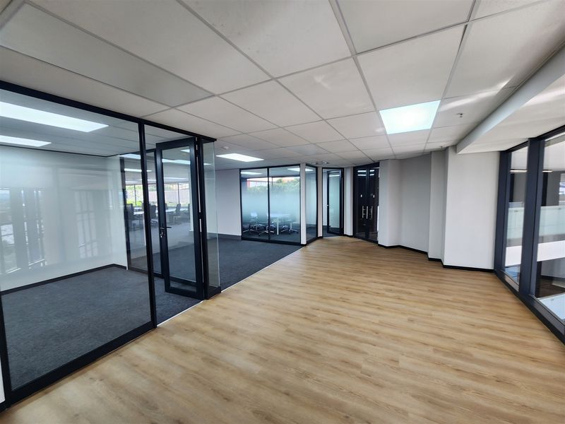 Modern open-plan office space featuring glass-partitioned meeting rooms, suspended ceilings, and a combination of laminate and carpet flooring.
