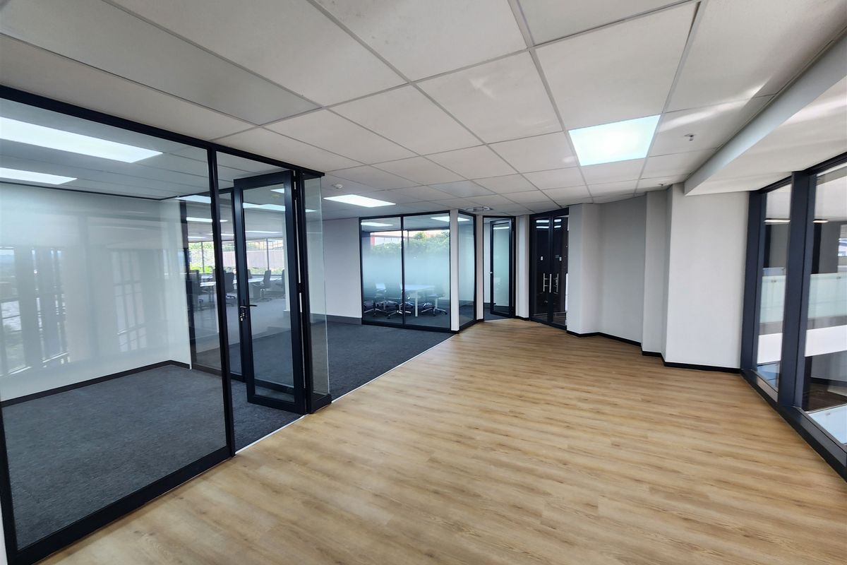 Modern open-plan office space featuring glass-partitioned meeting rooms, suspended ceilings, and a combination of laminate and carpet flooring.