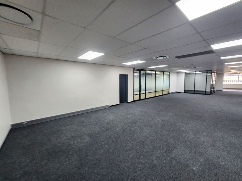Spacious open-plan office area featuring a suspended ceiling, recessed lighting, and modern glass partition walls, providing a clean and professional workspace.