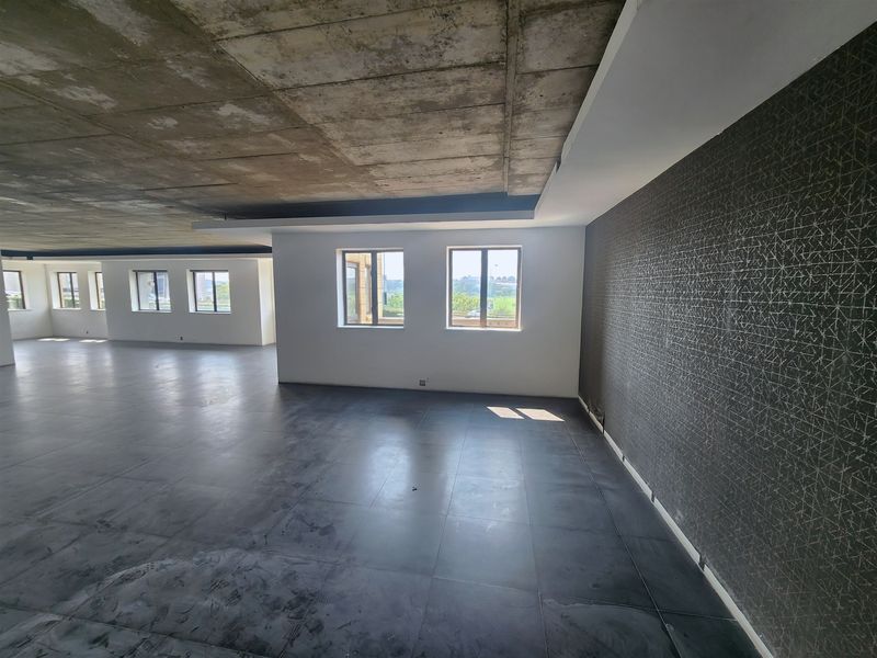Spacious open-plan office area featuring an exposed concrete ceiling, dark tiled flooring, and a modern textured feature wall with ample natural light.