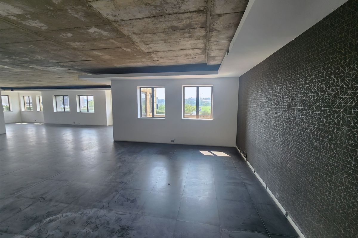 Spacious open-plan office area featuring an exposed concrete ceiling, dark tiled flooring, and a modern textured feature wall with ample natural light.