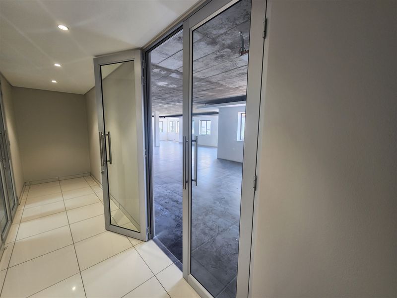 Spacious open-plan office area featuring modern aluminium glass doors, tiled flooring, and an industrial-style exposed concrete ceiling.