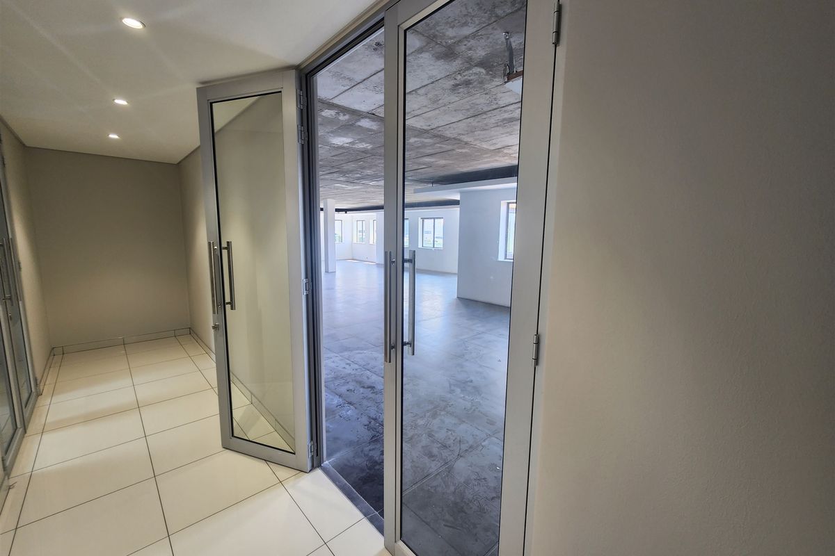 Spacious open-plan office area featuring modern aluminium glass doors, tiled flooring, and an industrial-style exposed concrete ceiling.