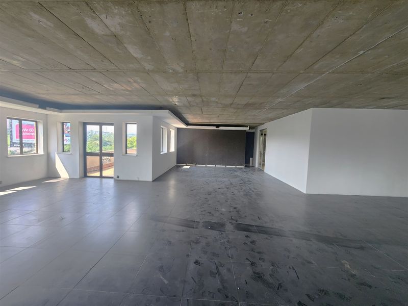 Spacious open-plan office area featuring an exposed concrete ceiling, large windows providing natural light, and tiled flooring.