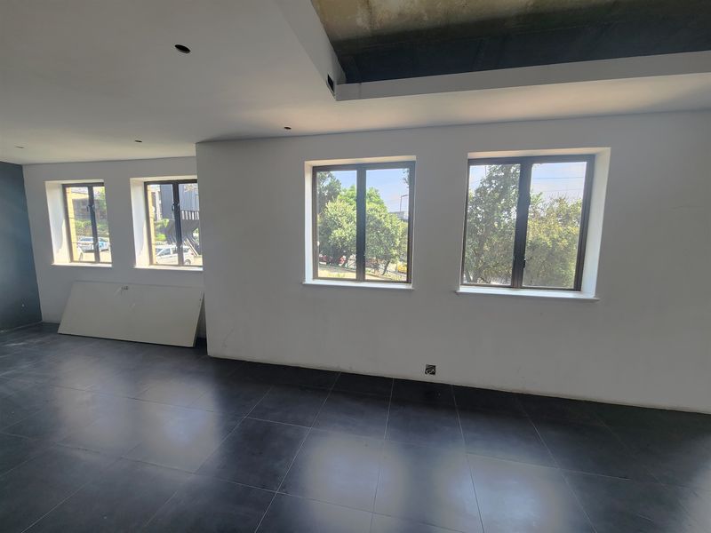 An empty office space featuring dark tiled flooring, large windows providing natural light, and an unfinished ceiling section awaiting final completion.